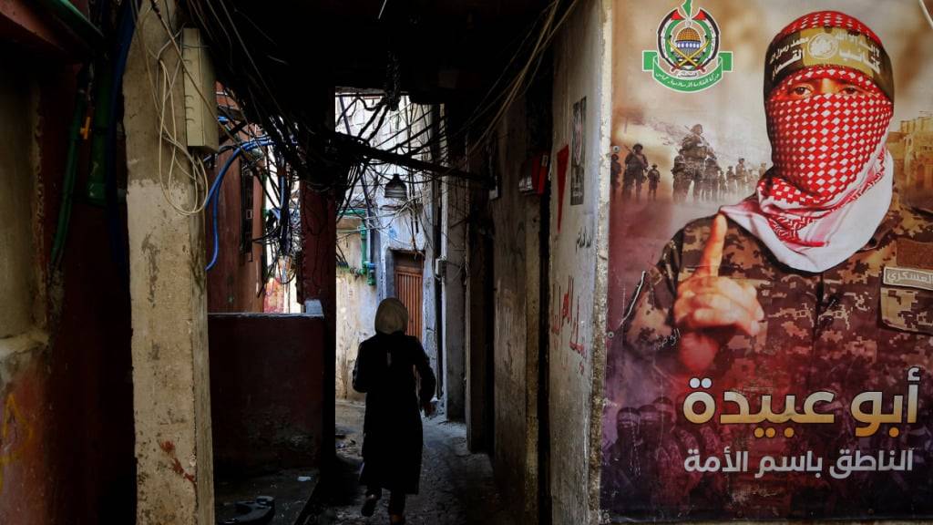 ARCHIV - Ein palästinensischer Flüchtling geht durch eine enge Gasse im Beiruter Lager Burj el-Barjneh, in der ein Plakat von Abu Obeida, dem Sprecher der Kassam-Brigaden, hängt. Foto: Marwan Naamani/dpa (Archivbild)