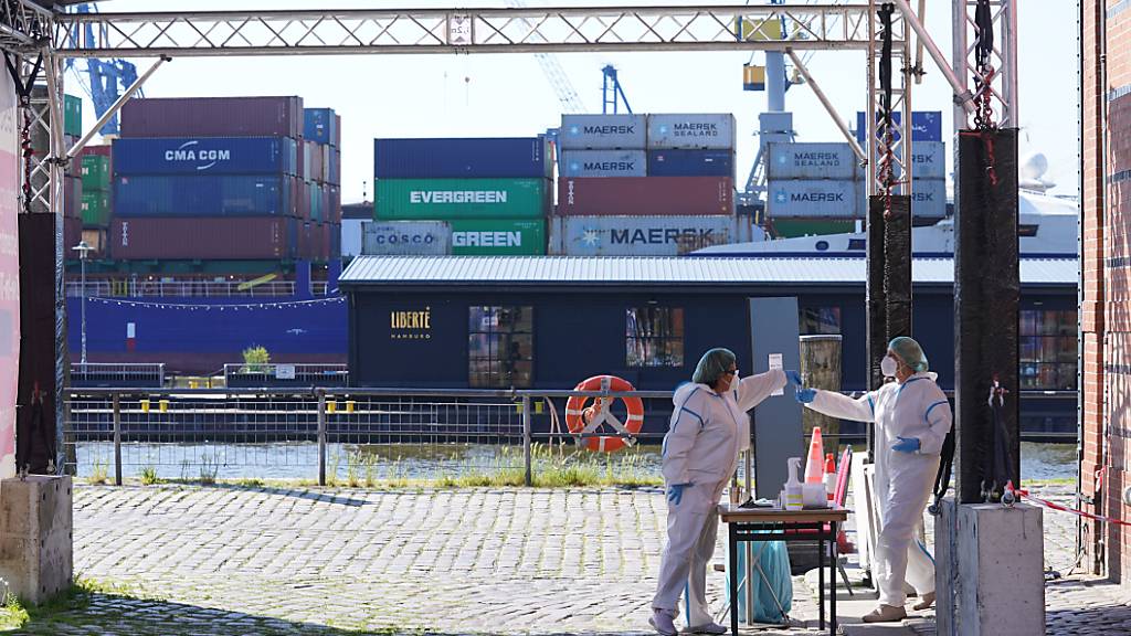 Eine Mitarbeiterin einer Corona-Schnelltest Drive-in-Station im Hafen überreicht einer Kollegin eine Testprobe. Foto: Marcus Brandt/dpa