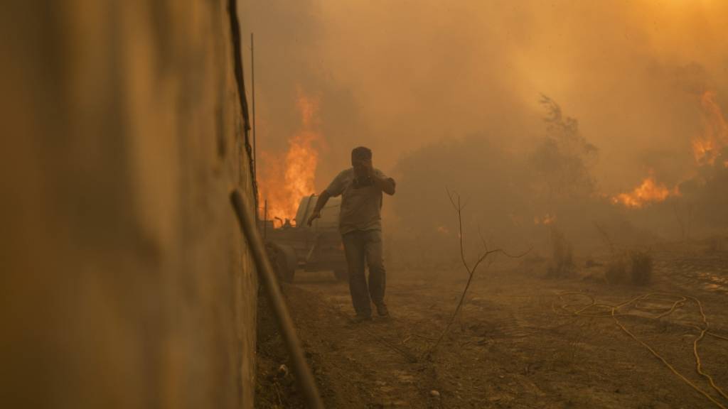 Ein Einheimischer flieht vor den Flammen von einem Waldbrand im Dorf Gennadi auf der griechischen Insel Rhodos. Foto: Petros Giannakouris/AP/dpa