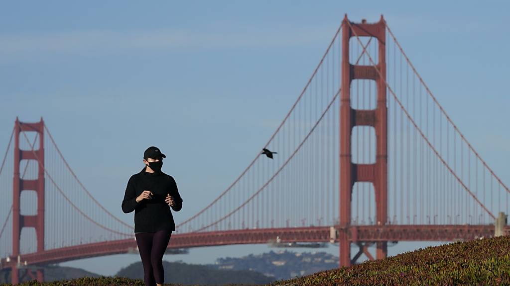 Eine Frau mit Mund-Nasen-Schutz läuft auf einem Weg vor der Golden Gate Bridge. Foto: Jeff Chiu/AP/dpa