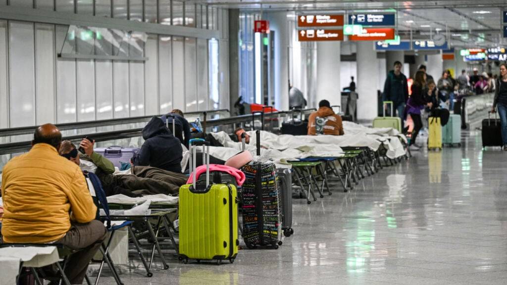 Menschen warten nach Drohnensichtungen und Flugausfällen in Flughafen München auf Feldbetten. Wegen Drohnensichtungen sind am Flughafen in München am Donnerstagabend rund 20 Flüge ausgefallen. Foto: Jason Tschepljakow/dpa