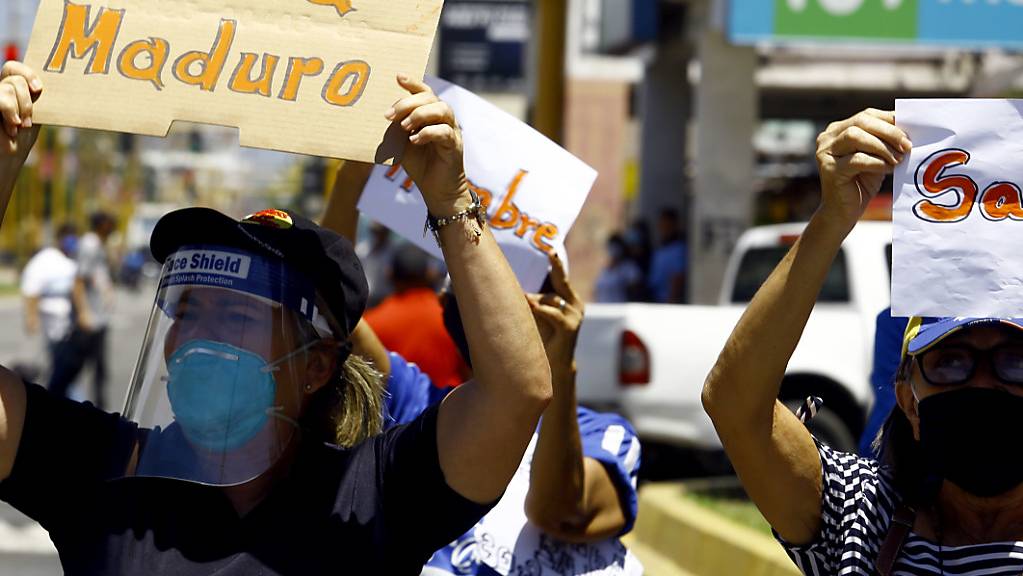 Eine Frau mit Mund-Nasen-Schutz hält bei einer Demonstration in Valencia ein Plakat mit der Aufschrift «Fuera Maduro» (Raus mit Maduro) in die Höhe. Foto: Juan Carlos Hernandez/ZUMA Wire/dpa