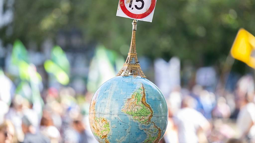 ARCHIV - Einen Globus mit einem Miniatur-Eiffelturm und dem 1,5-Grad Ziel des Pariser Klimaschutzabkommens trägt ein Mann auf der Demonstration vor der Alten Oper in Frankfurt. Foto: Boris Roessler/dpa