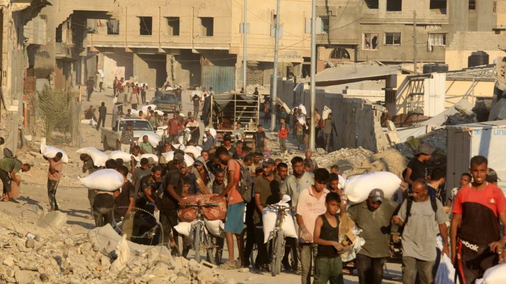 Palästinenser tragen Mehlsäcke entlang einer Straße in Chan Junis, nachdem Lastwagen mit humanitärer Hilfe über den von Israel kontrollierten Grenzübergang Kerem Shalom in den südlichen Gazastreifen eingefahren sind. Foto: Abed Rahim Khatib/dpa