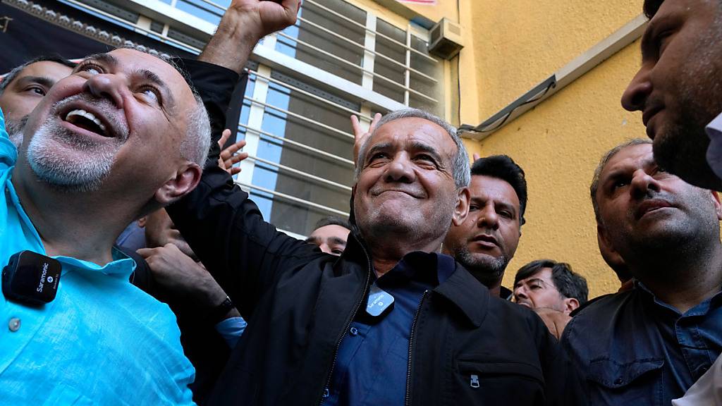 ARCHIV - Reformkandidat für die iranischen Präsidentschaftswahlen, Massud Peseschkian (M), ballt seine Faust, nachdem er seine Stimme in einem Wahllokal in Shahr-e-Qods bei Teheran abgegeben hat. Begleitet wird er vom ehemaligen Außenminister Mohammed-Dschawad Sarif links. Foto: Vahid Salemi/AP/dpa