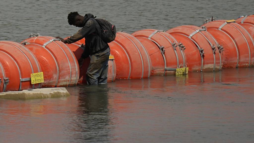 ARCHIV - Ein Mensch aus Kolumbien steht an einer schwimmenden Bojenbarriere, um den Rio Grande von Mexiko in die USA zu überqueren. Foto: Eric Gay/AP/dpa