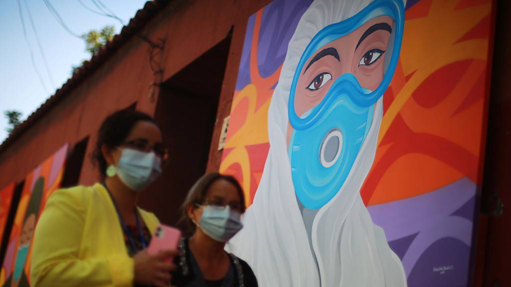 Zwei Frauen mit Masken gehen an einem Wandgemälde zur Anerkennung der Mitarbeiter des Gesundheitswesens bei der Bekämpfung des Covid-19 vorbei. (Archivbild) Foto: Jose Francisco Zuniga/Agencia Uno/dpa