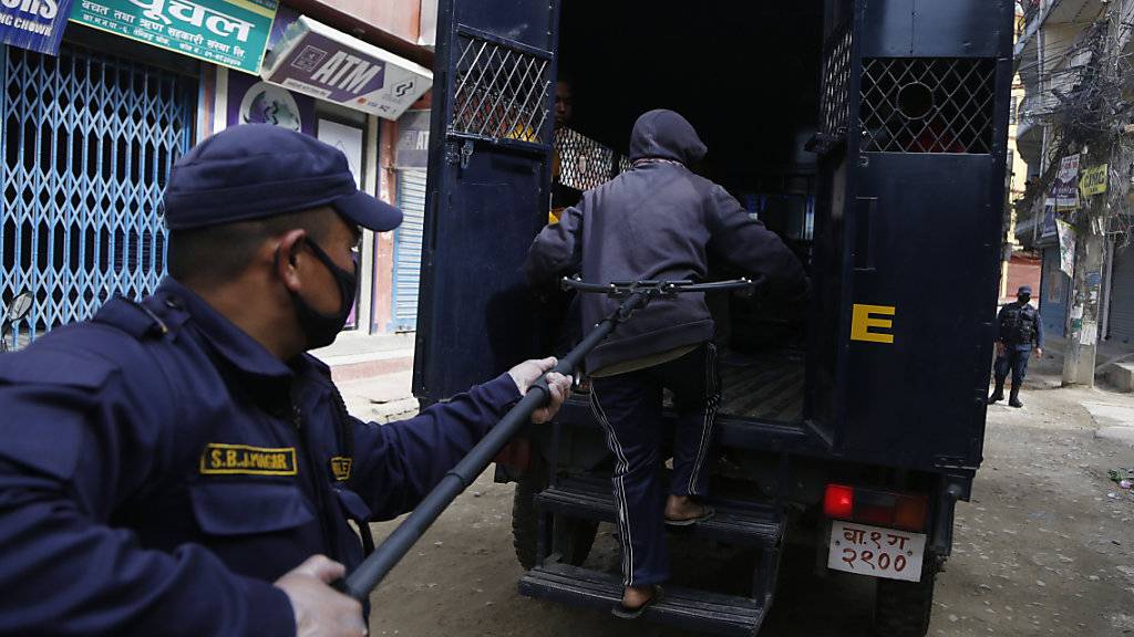 Ein Polizist in Nepal nimmt eine Person fest, die gegen die Ausgangssperre verstossen hat. Wegen der Corona-Pandemie benutzt die Polizei in Nepal lange Klammern.