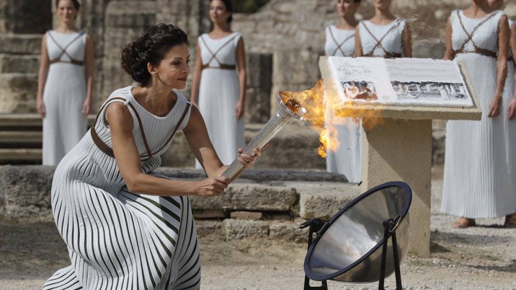 Eine Schauspielerin entfacht das olympische Feuer während der Zeremonie im antiken Olympia in Griechenland