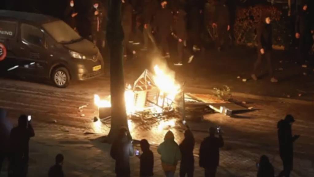 Schaulustige filmen mit ihren Handys brennende Gegenstände auf einer Straße in Haarlem. Erneut kam es in mehreren Städten in den Niederlanden zu Protesten. Foto: Uncredited/Mizzle Media/AP/dpa