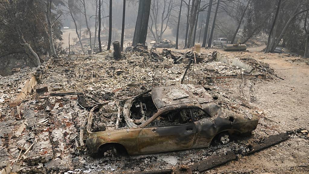 Ein ausgebranntes Auto steht in der Nähe eines Waldes. Etwas kühlere Temperaturen nach einer Hitzewelle haben die Löscharbeiten der US-Feuerwehr bei den Waldbränden in Kalifornien begünstigt. Foto: Marcio Jose Sanchez/AP/dpa