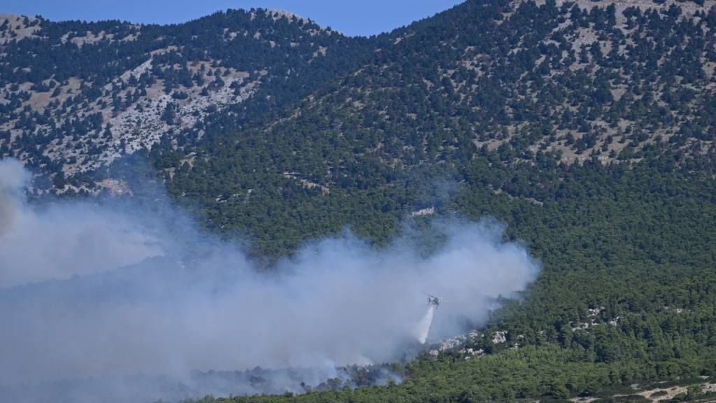 dpatopbilder - Ein Löschhubschrauber wirft bei einem Waldbrand nordwestlich von Athen Wasser über einem rauchverhangenen Wald ab. Foto: Michael Varaklas/AP/dpa