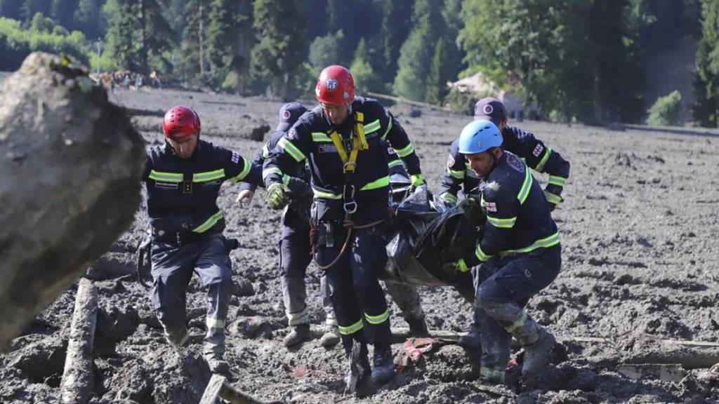 HANDOUT - Rettungskräfte tragen die Leiche des Opfers eines Erdrutsches in der Nähe von Schowi. Infolge eines Erdrutsches sind in einem Ferienort in Georgien im Kaukasusgebirge offiziellen Angaben zufolge mindestens elf Menschen ums Leben gekommen. Foto: Uncredited/Ministry of Internal Affairs of Georgia Press Service/AP/dpa - ACHTUNG: Nur zur redaktionellen Verwendung und nur mit vollständiger Nennung des vorstehenden Credits