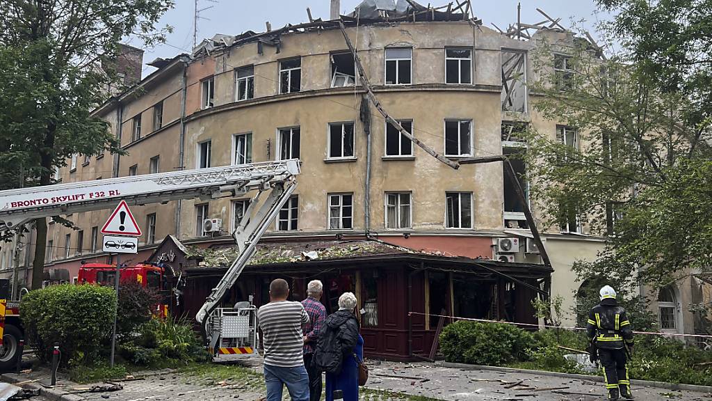 Menschen beobachten einen Feuerwehreinsatz nach einem Raketenangriff, bei dem ein Gebäude beschädigt wurde. Foto: Mstyslav Chernov/AP/dpa