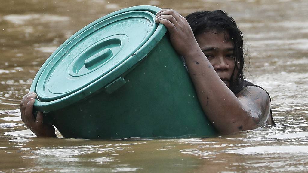 Eine Anwohnerin hält sich an einen Plastikbehälter als Schwimmboje fest, während sie in dem steigenden Hochwasser schwimmt. Foto: Aaron Favila/AP/dpa