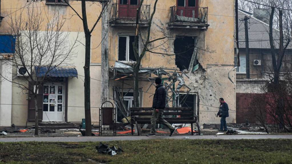 Personen gehen an einem beschädigten Wohnhaus in Mariupol vorbei. Die Evakuierung von Menschen aus der Hafenstadt ist nach ukrainischen Angaben verschoben worden. Die «russische Seite» halte sich nicht an die Waffenruhe, teilte die Stadt am Samstagmittag im Nachrichtenkanal Telegram mit. 