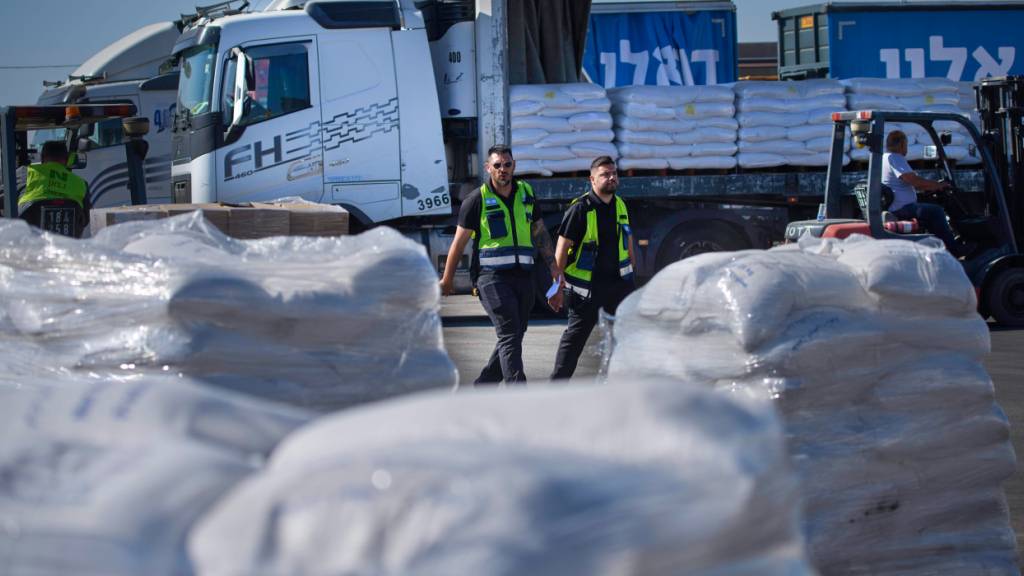 Arbeiter gehen an einem Lastwagen mit humanitärer Hilfe für den Gazastreifen vorbei, der am Entladebereich des Grenzübergangs Kerem Shalom zwischen Israel und dem Gazastreifen im Süden Israels geparkt ist. Foto: Ohad Zwigenberg/AP/dpa