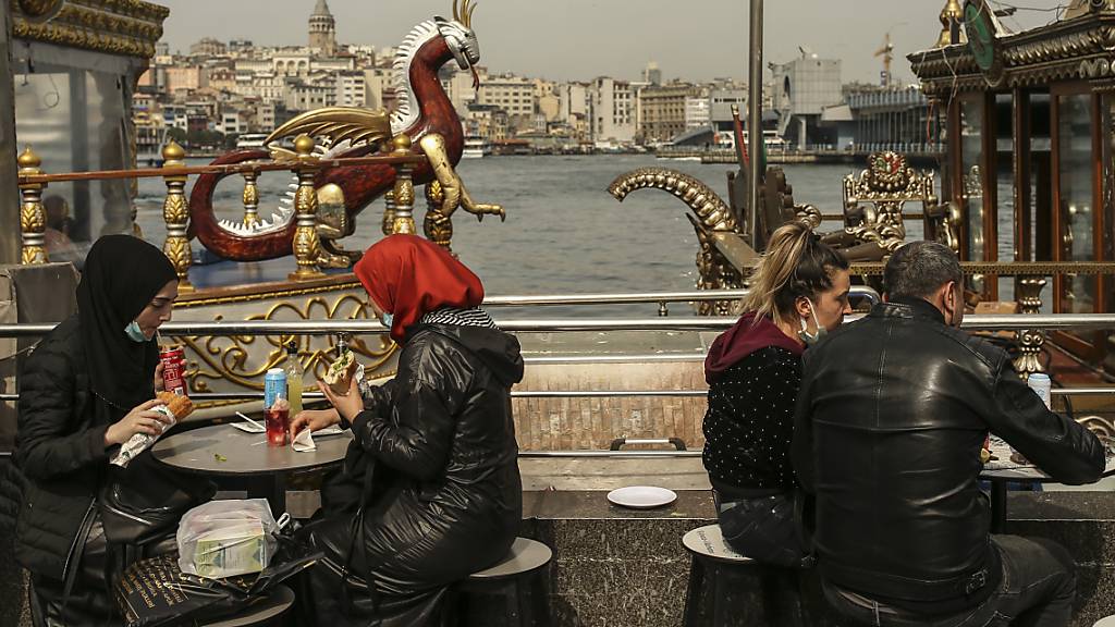 Menschen essen an Tischen am Ufer vom Goldenen Horn auf dem Eminonu Markt in Istanbul. Foto: Emrah Gurel/AP/dpa