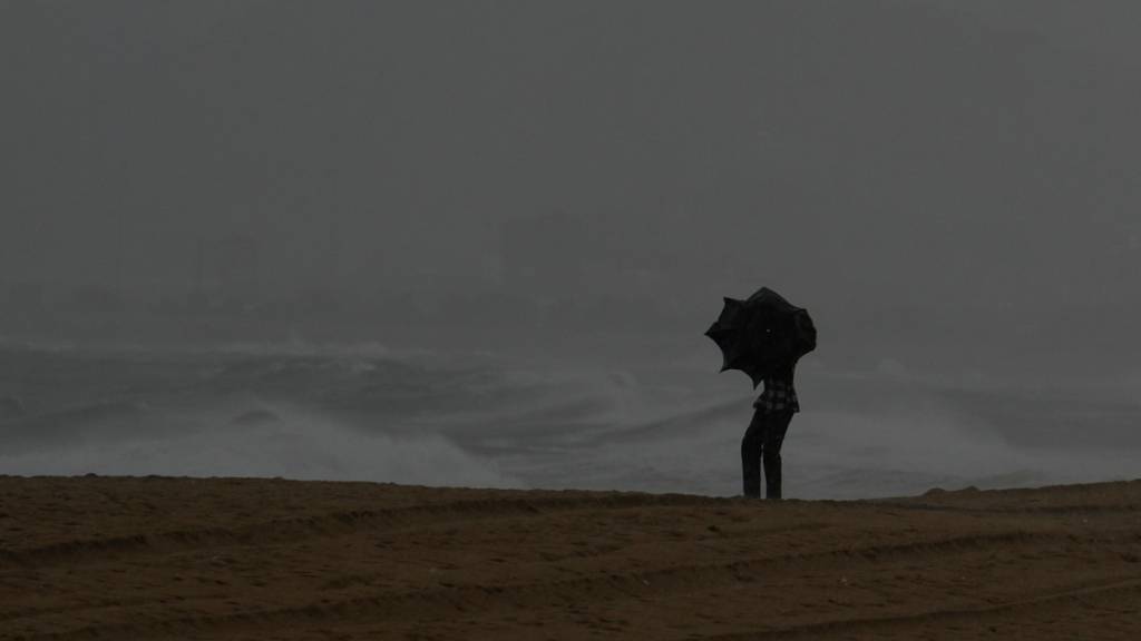 Ein Besucher hält einen Regenschirm am Ramakrishna-Strand in Indien. Foto: Mahesh Kumar A./AP/dpa
