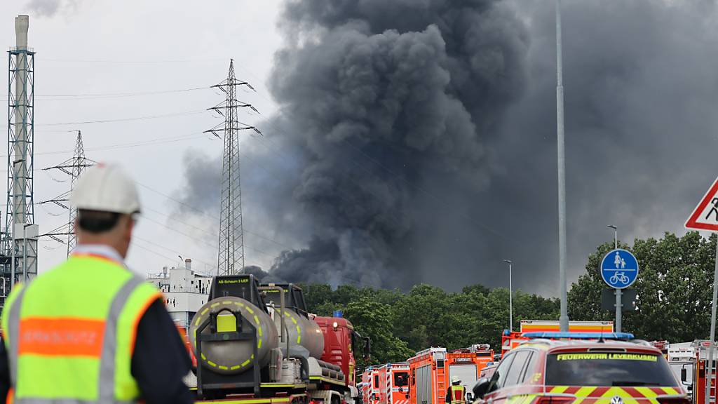 dpatopbilder - Einsatzfahrzeuge der Feuerwehr stehen unweit einer Zufahrt zum Chempark über dem eine dunkle Rauchwolke aufsteigt. Foto: Oliver Berg/dpa