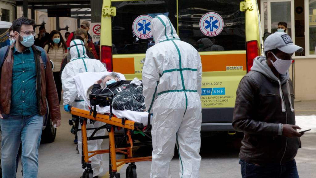 Medizinische Mitarbeiter in Schutzausrüstung transportieren einen Patienten auf einer Trage, um ihn in einem Krankenhaus in Athen zu verlegen. Foto: Marios Lolos/Xinhua/dpa