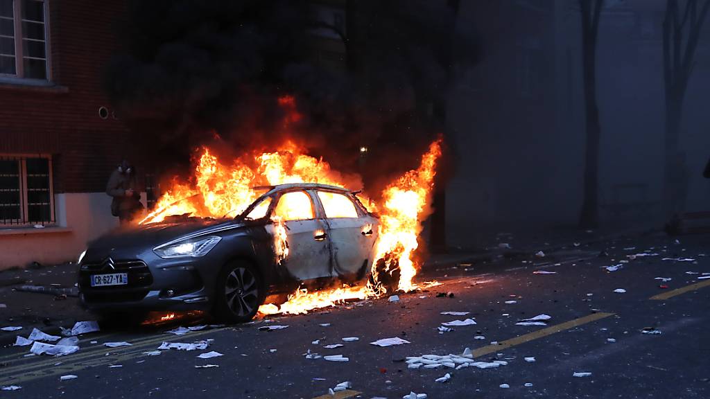 Ein brennendes Fahrzeug steht während einer Demonstration auf einer Straße. Der Protest bezieht sich auf Aufnahmen eines Vorfalls im vergangenen Monat, bei dem Polizisten einen Schwarzen geschlagen haben sollen. Foto: Francois Mori/AP/dpa