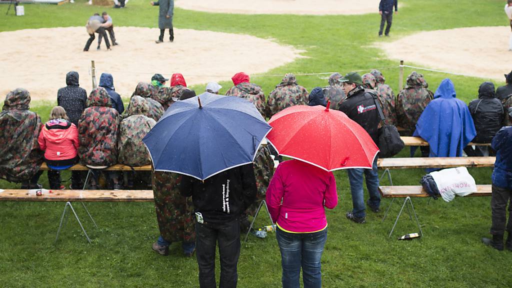 Besucher eines Schwingfests unter Regenschirmen