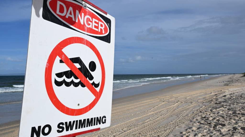 ARCHIV - Ein Schild mit der Aufschrift «Gefahr - Schwimmen verboten» steht an dem Strand Woorim Beach auf Bribie Island. Foto: Darren England/AAP/dpa