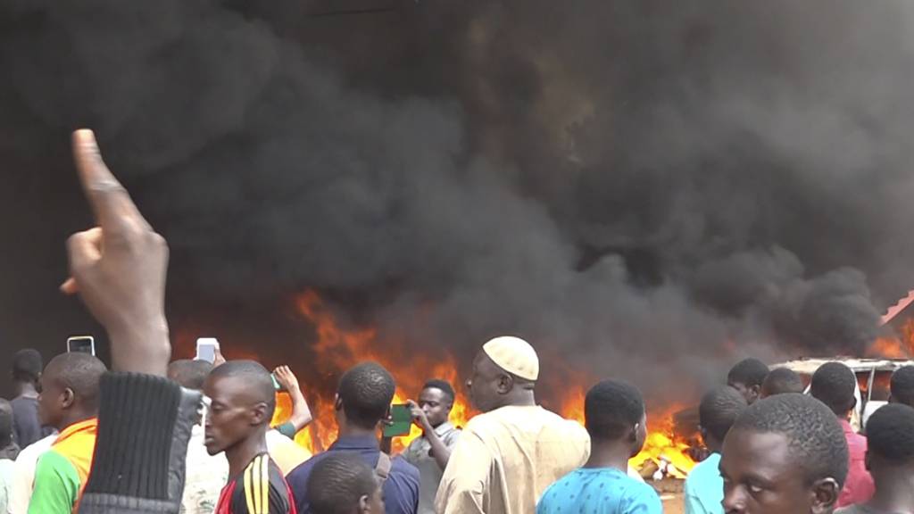 dpatopbilder - Mit dem brennenden Hauptquartier der Regierungspartei im Rücken demonstrieren Anhänger meuternder Soldaten. Das Militär im Niger hat erklärt, die Forderung der Putschisten nach einem Ende der Amtszeit von Präsident Bazoum zu unterstützen. Foto: Fatahoulaye Hassane Midou/AP/dpa