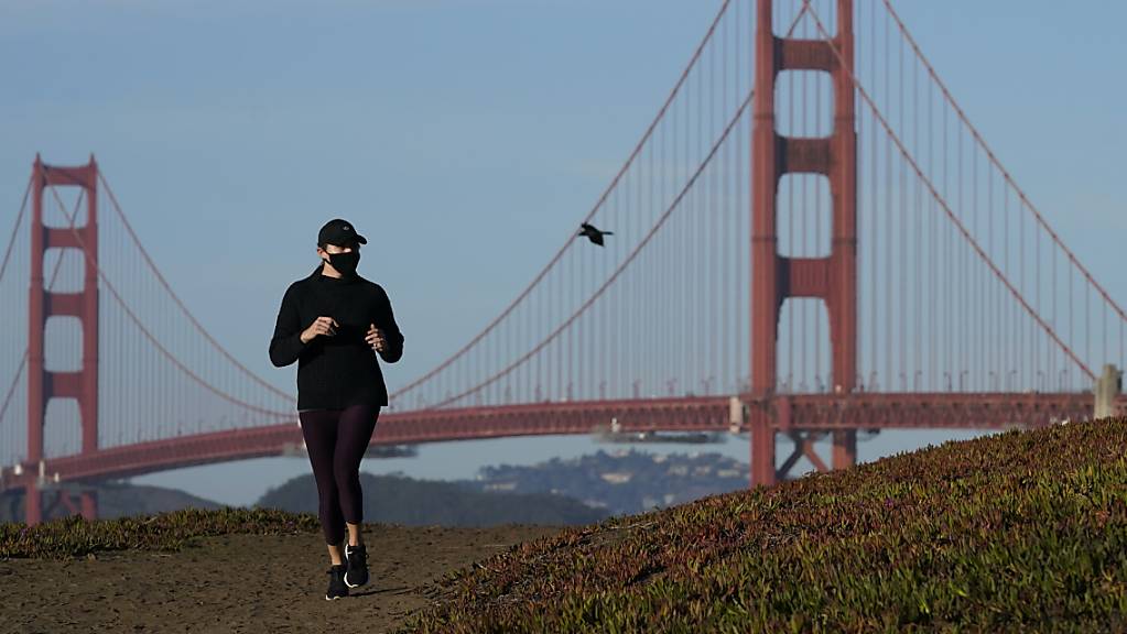 Eine Frau mit Mund-Nasen-Schutz joggt unweit der Golden Gate Bridge in San Francisco. In fünf Bezirken in der Region sind die Bewohner dazu angehalten, ihr Zuhause nicht zu verlassen. Foto: Jeff Chiu/AP/dpa