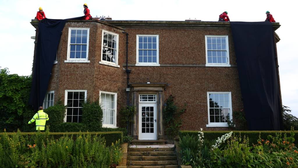 HANDOUT - Ein von Greenpeace herausgegebenes Foto zeigt Aktivisten, die ein Haus verhüllen. Foto: Luca Marino/Greenpeace/PA Media/dpa - ACHTUNG: Nur zur redaktionellen Verwendung im Zusammenhang mit der aktuellen Berichterstattung bis maximal 17.08.2023 und nur mit vollständiger Nennung des vorstehenden Credits. Kein Verkauf, keine Archivierung.