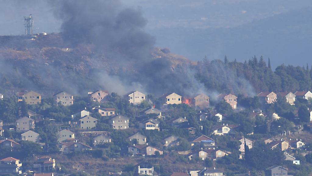 ARCHIV - Feuer und schwarzer Rauch steigen zwischen den Häusern der nördlichen israelischen Grenzstadt Metula auf, die von der Hisbollah beschossen wurde, fotografiert aus Marjayoun im Südlibanon. Foto: Hussein Malla/AP/dpa
