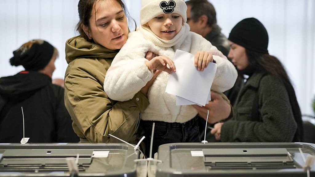 Eine Frau hält ein Kind während der Stimmabgabe. Foto: Vadim Ghirda/AP