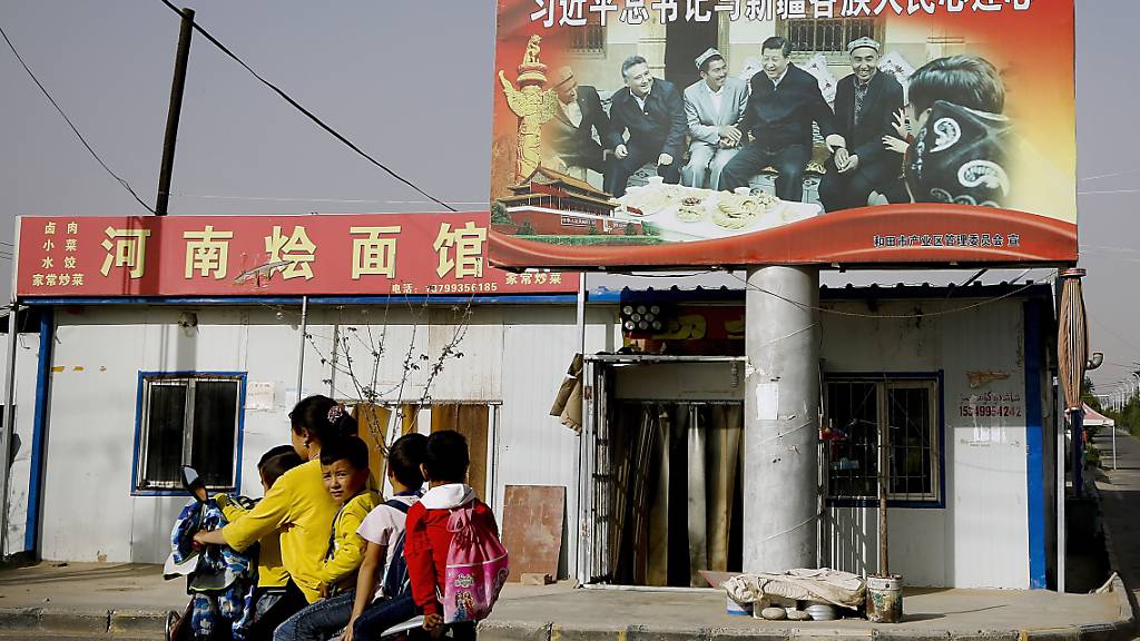 ARCHIV - Eine uigurische Frau fährt mit Schulkindern an einem Bild von Chinas Präsident Xi Jinping und einer Gruppe von uigurischen Ältesten vorbei. 43 Nationen haben am Donnerstag in einer UN-Vollversammlung Menschenrechtsverletzungen Chinas unter anderem an den Uiguren in der Region Xinjiang verurteilt. Foto: Andy Wong/AP/dpa