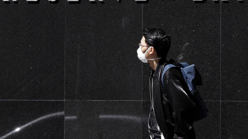 Ein Mann mit einer Maske vor dem Gebäude der australischen Notenbank in Sydney. (Archivbild)