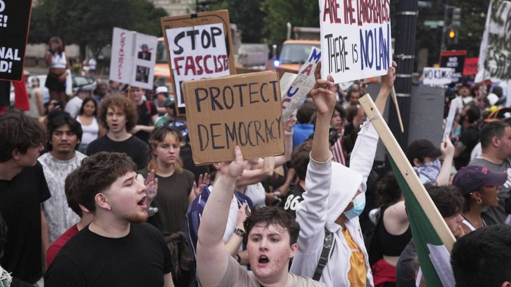 Menschen demonstrieren während einer Militärparade, anlässlich des 250-jährigen Bestehens des US-Heeres, das mit dem 79. Geburtstag von US-Präsident Trump zusammenfällt. Foto: Evan Vucci/AP/dpa