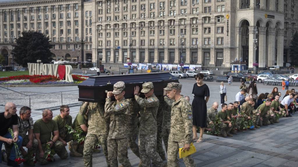Menschen in Kiew knien nieder, während Soldaten den Sarg eines Kameraden tragen, der in einem Gefecht getötet wurde. Foto: Efrem Lukatsky/AP/dpa