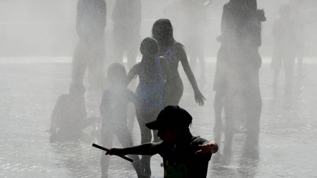 Menschen kühlen sich in Madrid bei heißem Wetter in einem Brunnen ab. Foto: Paul White/AP/dpa/Archiv