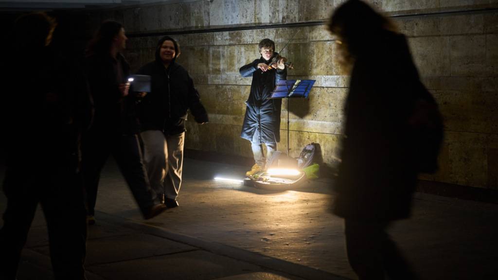 ARCHIV - Ein Straßenmusiker spielt Geige, während Menschen in einer U-Bahn-Querung während der Verdunkelungszeiten aufgrund der regelmäßigen russischen Luftangriffe in der ukrainischen Hauptstadt vorbeigehen. Foto: Efrem Lukatsky/AP/dpa