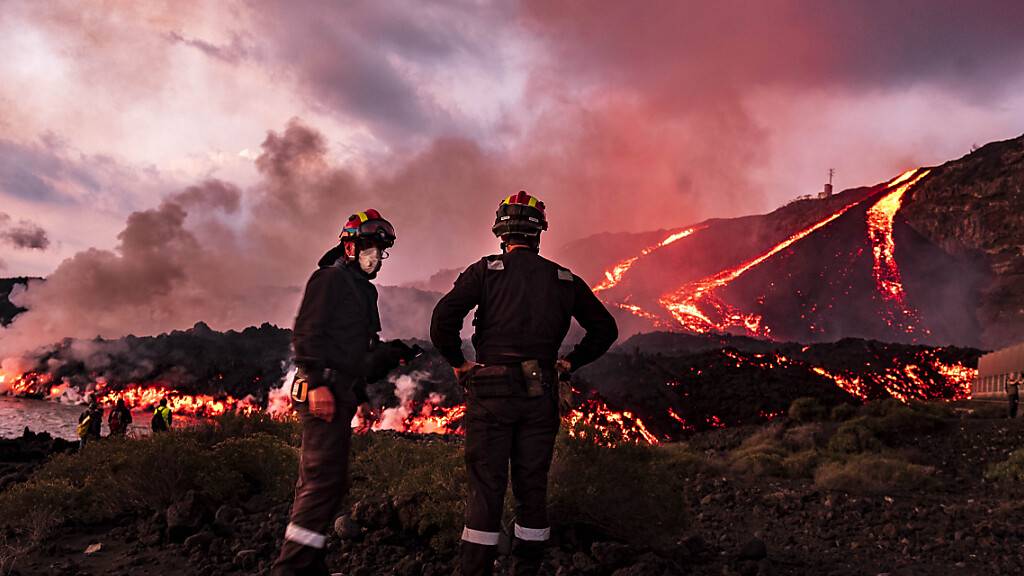 Mitglieder der militärischen Notfalleinheit (UME) sind im Einsatz, als Lava aus einem Vulkan ins Meer fließt. Auf der Kanareninsel La Palma spuckt seit neun Wochen der Vulkan Lava, Asche und Rauch aus. Ein Ende des verheerenden Ausbruchs ist immer noch nicht absehbar. Foto: Taner Orribo/AP/dpa