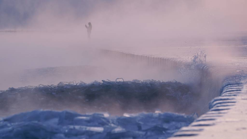 Eine Person spaziert über einen mit Eis bedeckten Strand am Ufer des Michigansees. Foto: Kiichiro Sato/AP/dpa