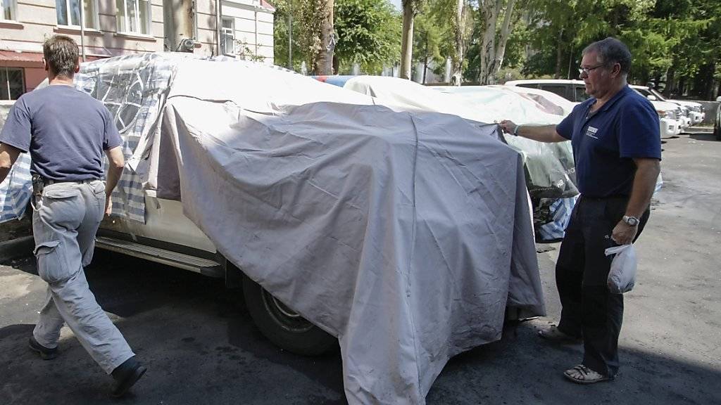 OSZE-Mitarbeiter inspizieren ein ausgebranntes Auto bei Donezk - am Wochenende gerieten Beobachter in der Ukraine ins Kreuzfeuer.