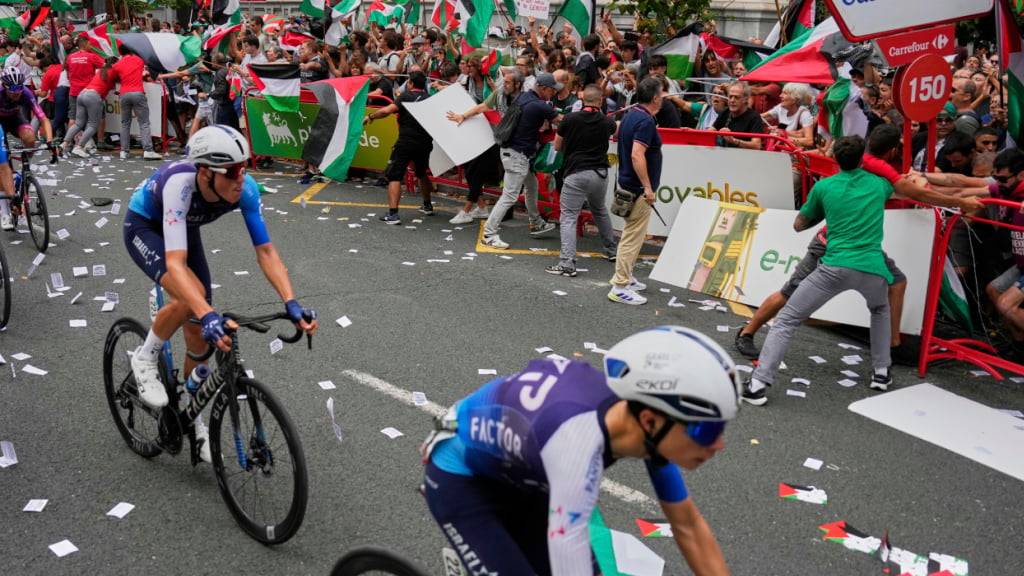 Radprofis des Teams Israel-Premier Tech fahren in Bilbao an der Stelle vorbei, wo sich viele propalästinensische Demonstranten versammelt haben - später muss die 11. Etappe der Spanien-Rundfahrt gar abgebrochen werden