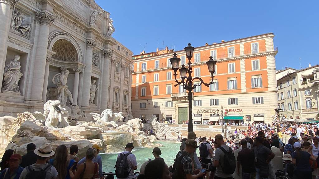 Touristen stehen im Schatten am Trevibrunnen (Fontana di Trevi)  auf der Piazza di Trevi. Foto: Robert Messer/dpa