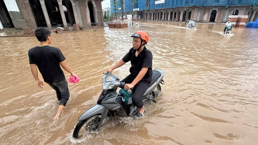 Menschen fahren Motorrad auf einer überfluteten Straße nach dem Taifun Kajiki. Foto: Hau Dinh/AP/dpa
