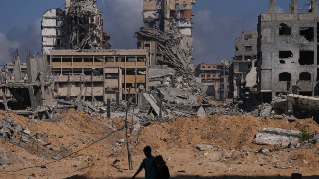 Palästinenser gehen an Häusern vorbei, die durch die israelische Luft- und Bodenoffensive zerstört wurden. Foto: Abdel Kareem Hana/AP/dpa