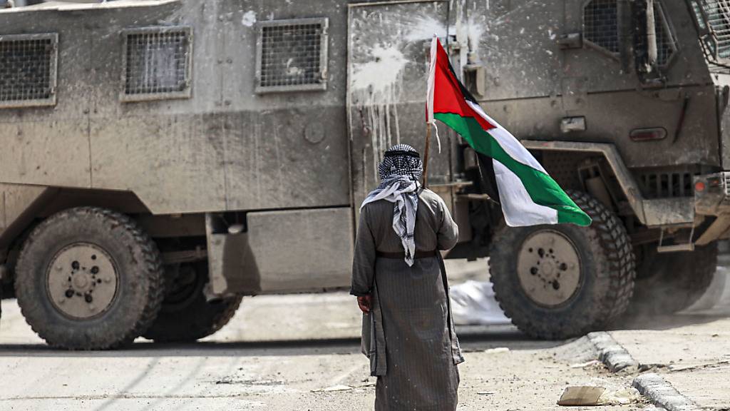 ARCHIV - Ein palästinensischer Mann steht mit einer palästinensischen Flagge in der Hand vor einem israelischen Militärfahrzeug. Foto: Nasser Ishtayeh/SOPA Images via ZUMA Press Wire/dpa