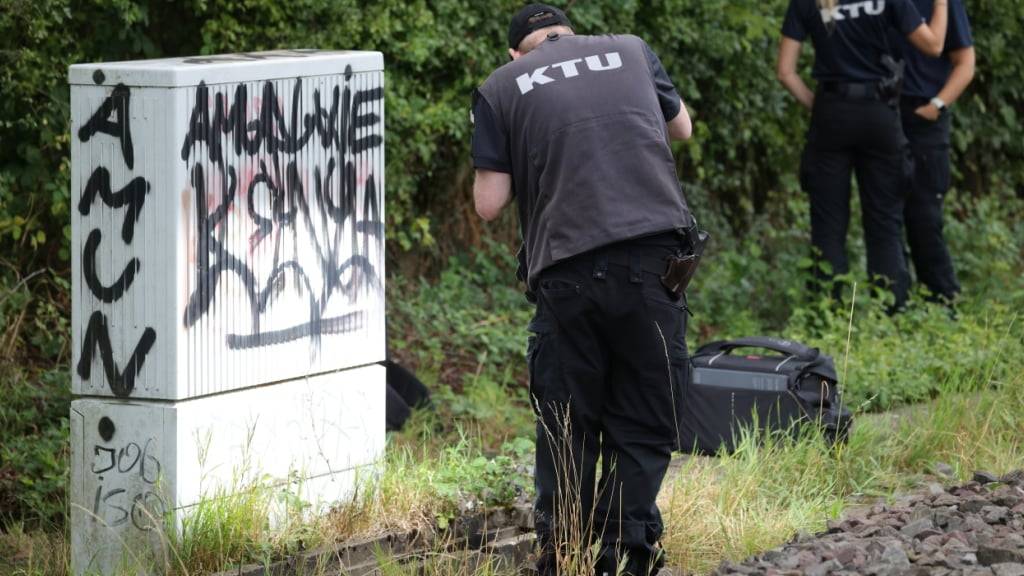 Ein Mitarbeiter der KTU (Kriminaltechnische Untersuchung) steht an «Betonwanne» am Rande der Bahngleise, in der sich verbrannte Kabel befinden. Auf die wichtige Nord-Süd-Strecke der Deutschen Bahn ist ein weiterer Brandanschlag verübt worden. Foto: Christoph Reichwein/dpa