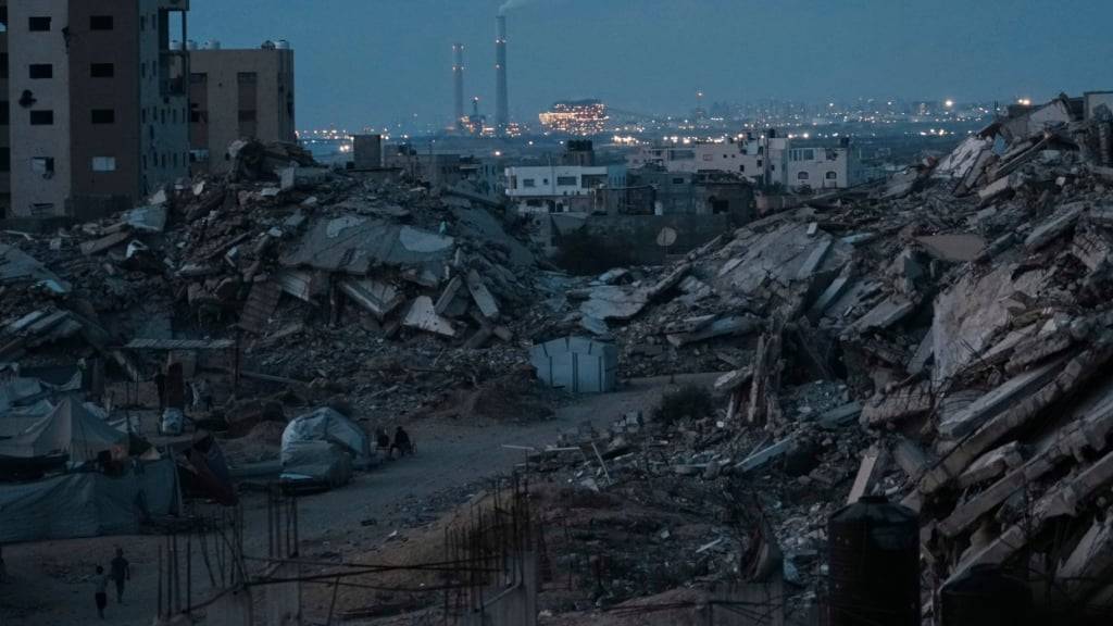 Palästinenser, die durch die israelische Luft- und Bodenoffensive auf den Gazastreifen vertrieben wurden, halten sich in der Abenddämmerung in einem Gebiet bei Gaza-Stadt umgeben von zerstörten Gebäuden auf. Foto: Jehad Alshrafi/AP/dpa