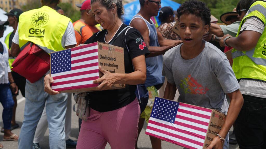 Von den Erdbeben betroffene Menschen tragen humanitäre Hilfsgüter aus den USA, nachdem sie diese erhalten haben. Foto: Ariana Cubillos/AP/dpa